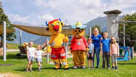 Group photo with children and mascots outdoors, surrounded by nature.