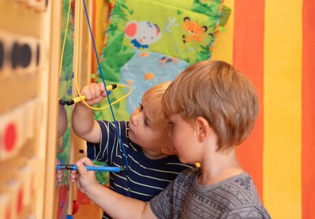 Zwei Kinder kreativ mit Stiften an einem Spielbrett.