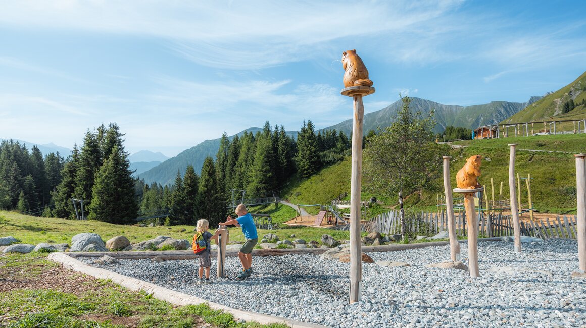 Two children play outdoors, surrounded by mountains and trees