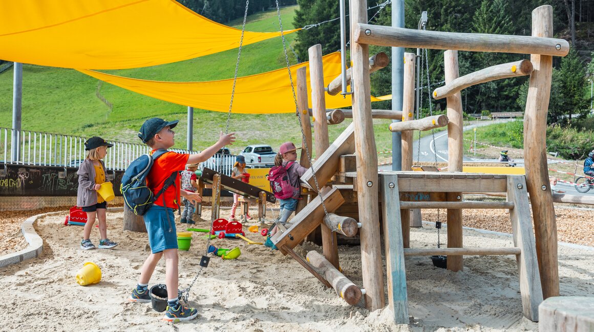 Three children are playing at a playground under a sunshade.