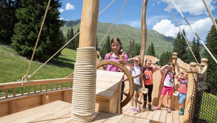 Vier kinderen spelen op een houten schip in de buitenlucht.