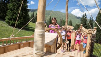 Four children playing on a wooden ship in the outdoors.
