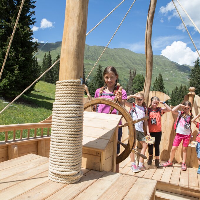 Four children playing on a wooden ship in the outdoors.