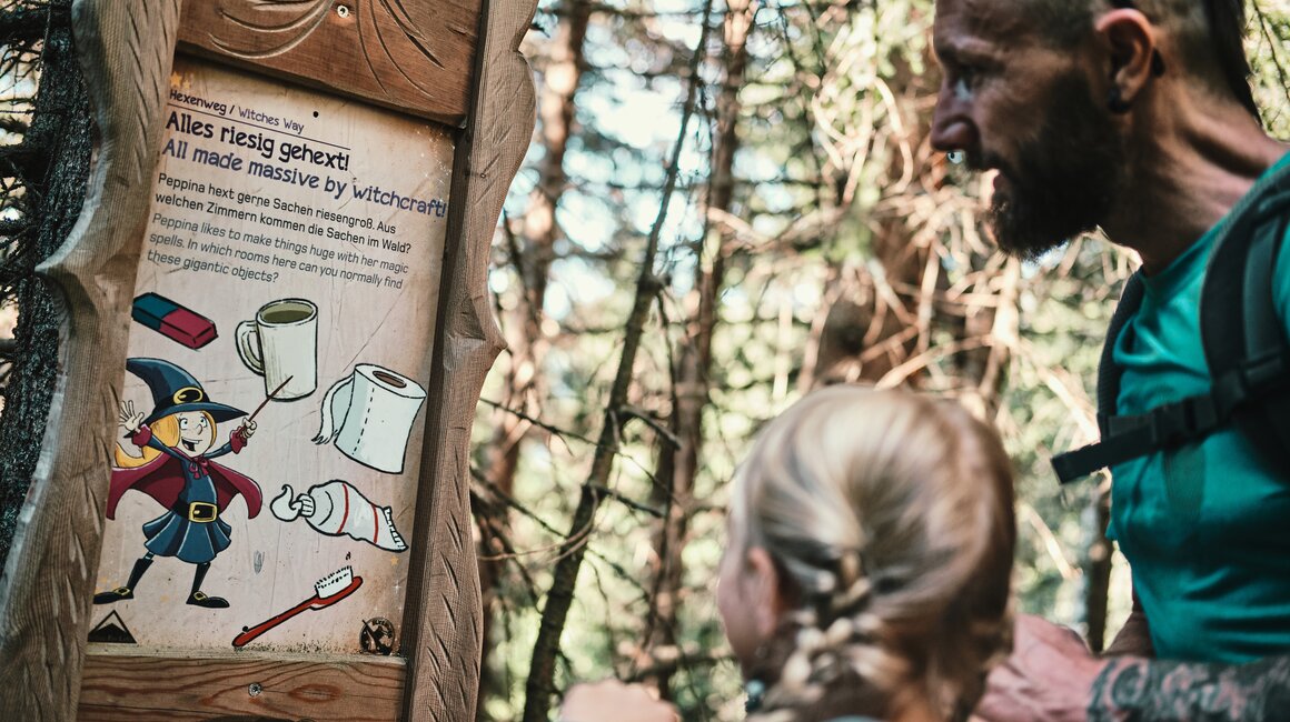 An adult and a child observing an information sign in the woods.