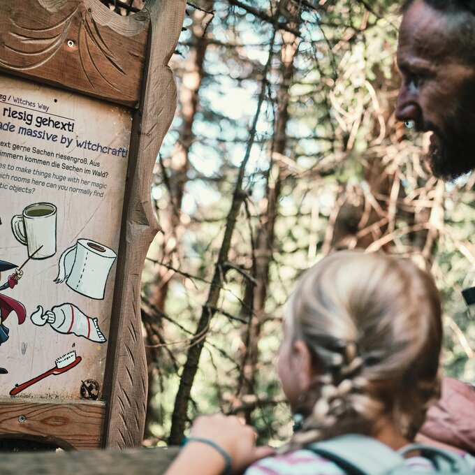 An adult and a child observing an information sign in the woods.