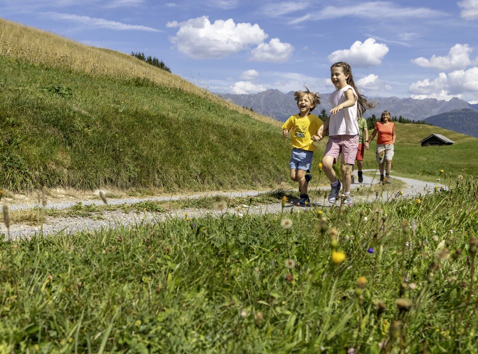 Four children joyfully running on a country path surrounded by flowers.