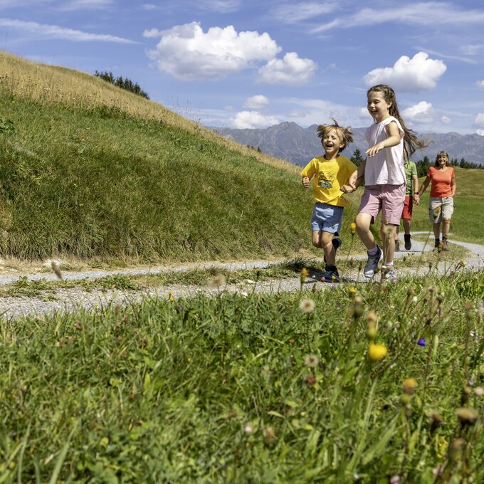 Four children joyfully running on a country path surrounded by flowers.