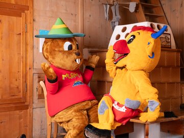 Two mascots sitting in a wooden room chatting.