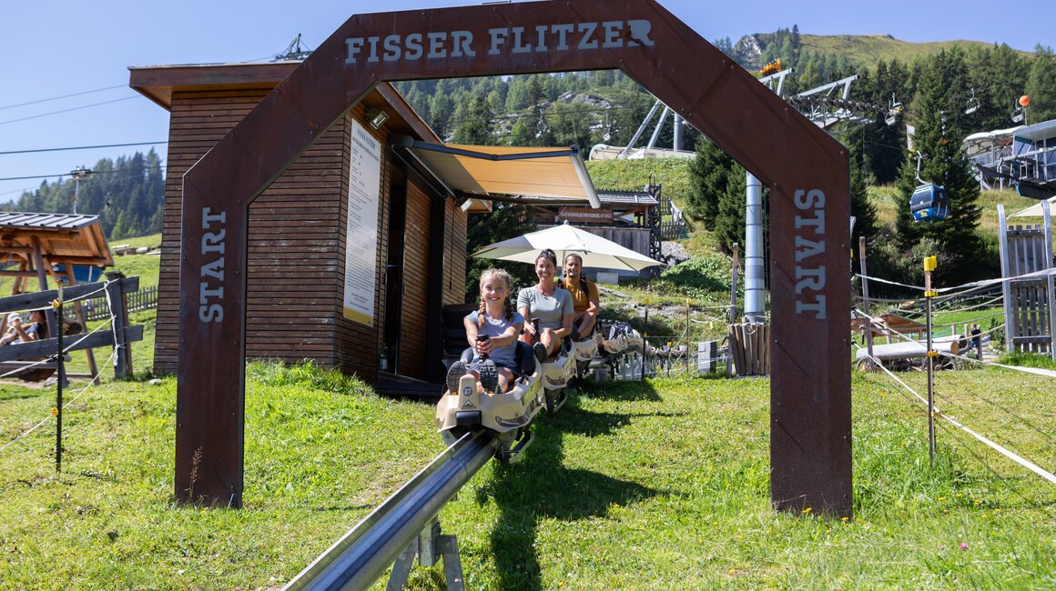 Two people riding the Fisser Flitzer summer toboggan in sunny weather.