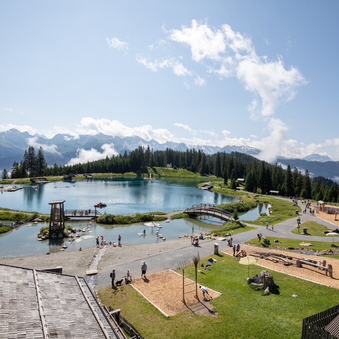 Families enjoy the day at a mountain lake with a playground and nature.