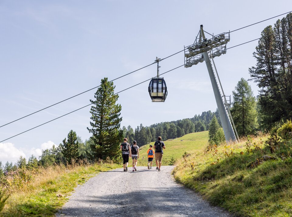 Three hikers walking on a path with cable car above.