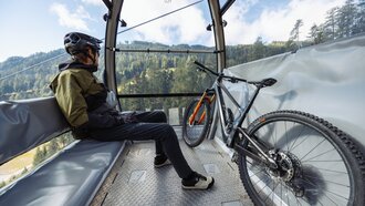 Man sitting with mountain bike in gondola on the way up.
