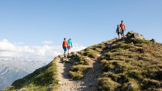 Zwei Wanderer gehen einen Bergpfad, umgeben von atemberaubender Berglandschaft.