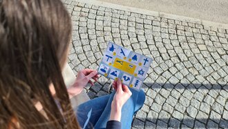 Eine Person schaut auf ein Blatt mit Symbolen auf Steinpflaster.