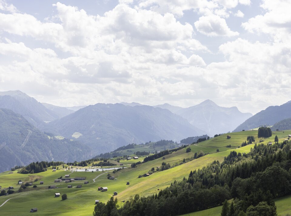 Blick auf grüne Wiesen und Berge unter bewölktem Himmel.