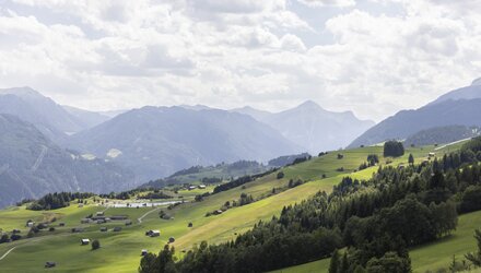 Blick auf grüne Wiesen und Berge unter bewölktem Himmel.
