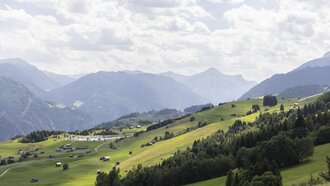 View of green fields and mountains under a cloudy sky.