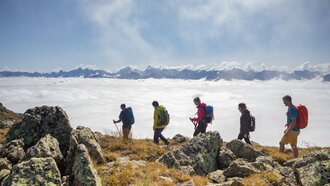 Five hikers explore a mountainous landscape above the clouds.