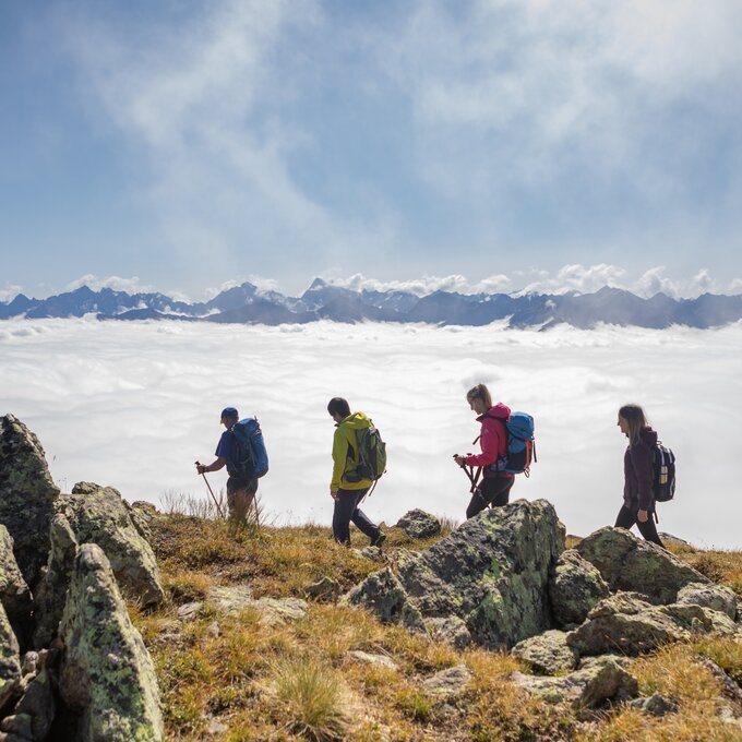 Fünf Wanderer erkunden eine bergige Landschaft über den Wolken.