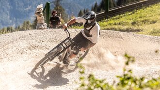A mountain biker swiftly turns on a trail, dust clouds around him.