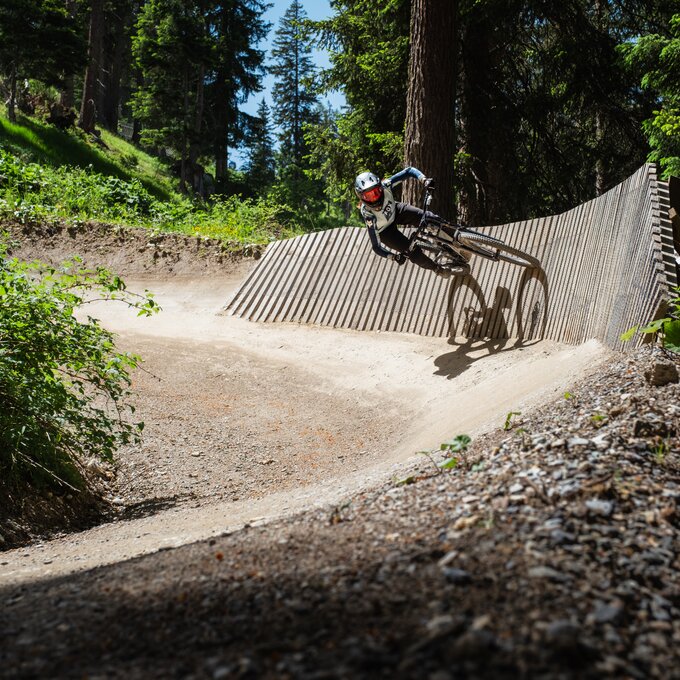 Ein Mountainbiker kurvt auf einer Holzpiste durch den Wald.