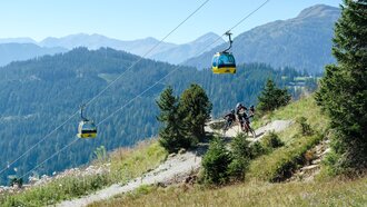 Zwei Mountainbiker nutzen die Strecke neben der Seilbahn in den Bergen.