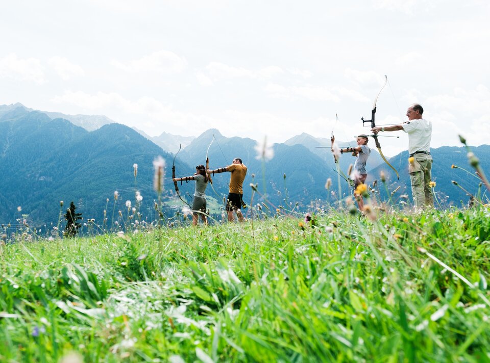Four people practicing archery on a mountain meadow.
