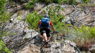 A climber ascends a steep rock face using iron grips and a cable.