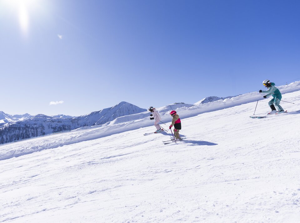 Drei Skifahrer genießen die Piste unter strahlend blauem Himmel.