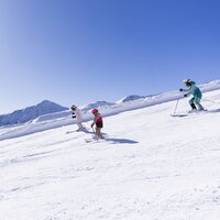 Drei Skifahrer genießen die Piste unter strahlend blauem Himmel.