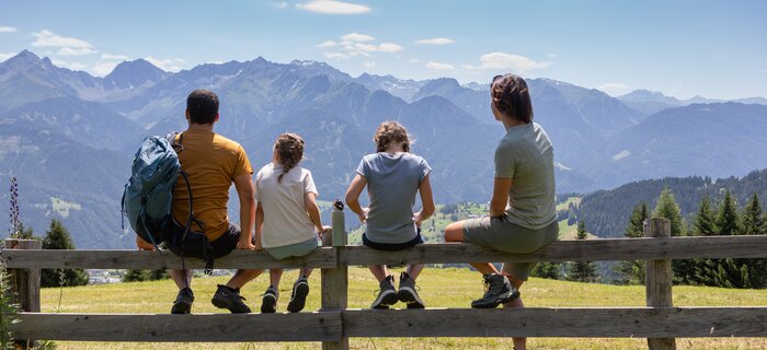 A family sits on a fence enjoying the mountain view.
