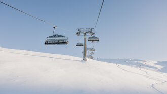 An empty ski lift moves over a snow-covered landscape.