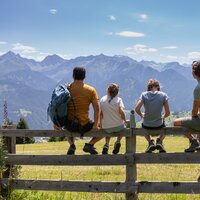 Eine Familie sitzt auf einem Zaun und genießt die Berglandschaft.