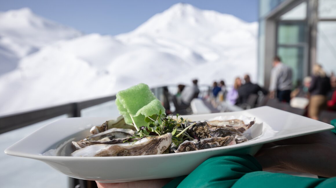 Ein Teller Austern mit grüner Garnitur vor schneebedeckten Bergen.