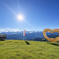 Ein Herz-Symbol und die Alpenlandschaft unter blauem Himmel.