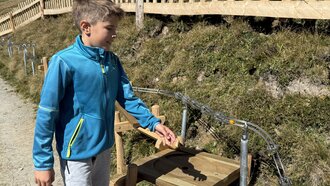 A boy watches others on a hiking path in the mountains.