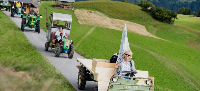 A tractor parade with various vehicles and drivers in the Alps.
