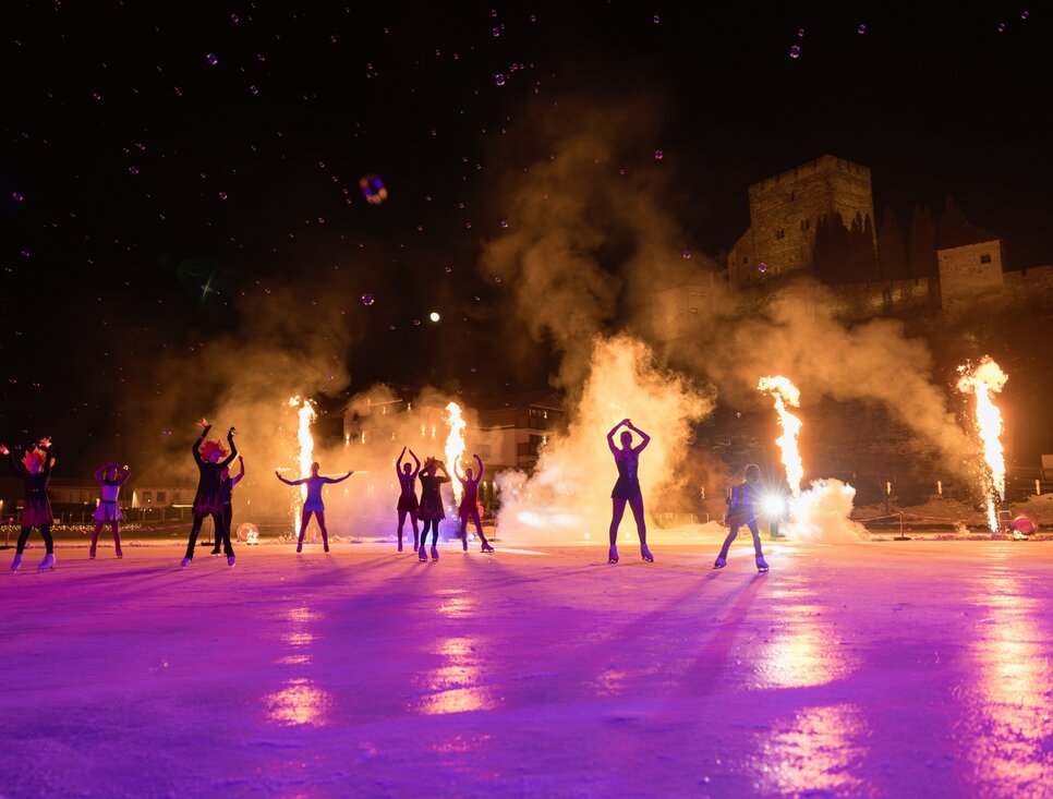 Performers create a captivating display on ice surrounded by fire effects.