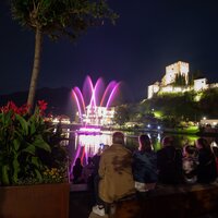 Besucher genießen eine Wasserlichtshow am See mit Schloss im Hintergrund.