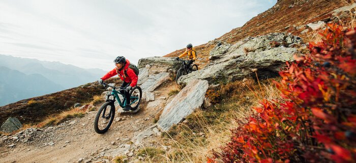 Two mountain bikers riding on a challenging trail in the mountains.