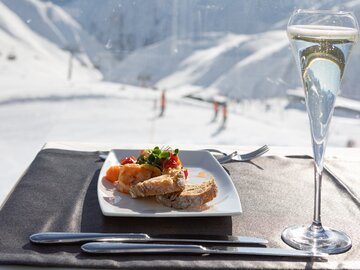 Ein elegantes Gericht mit Brot und Garnelen, Aussicht auf schneebedeckte Berge, dazu ein Glas Sekt.