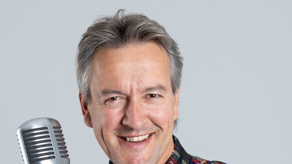 Ein Sänger lächelt und hält ein Mikrofon in der Hand.