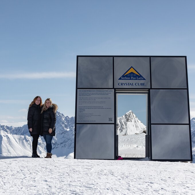 Zwei Frauen stehen im Crystal Cube in den Bergen, umgeben von Schnee.