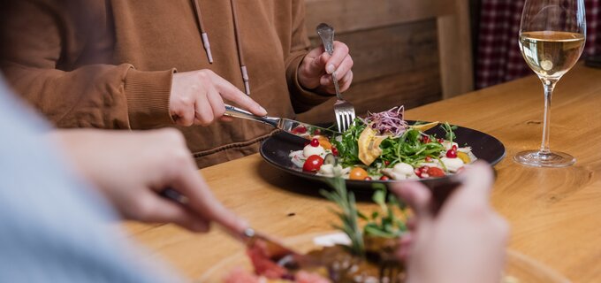 Zwei Personen speisen an einem Holztisch, mit Salat und Wein.