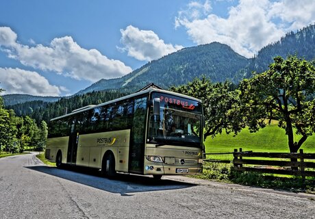Ein Postbus hält vor einer idyllischen Berglandschaft mit Bäumen.
