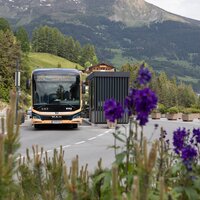 Een bus die een bushalte nadert met op de achtergrond bergen.