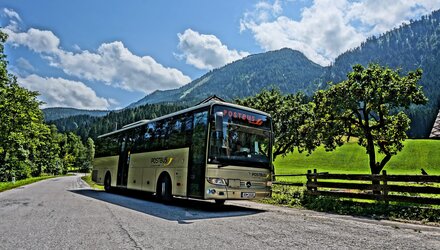 Ein Postbus hält an einer kurvenreichen Straße in den Bergen.
