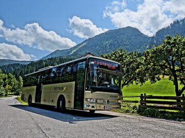 A postbus stops on a winding road in the mountains.