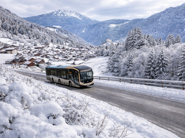 Een bus reist door een besneeuwde omgeving met bergen op de achtergrond.