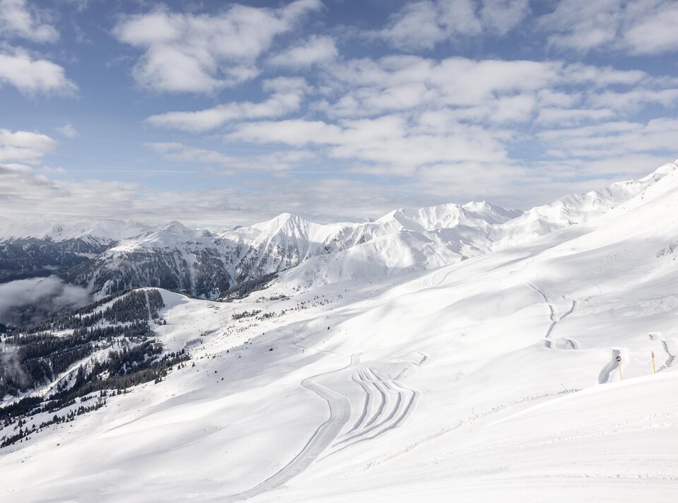 Wide snow-covered mountain landscape under cloudy sky.